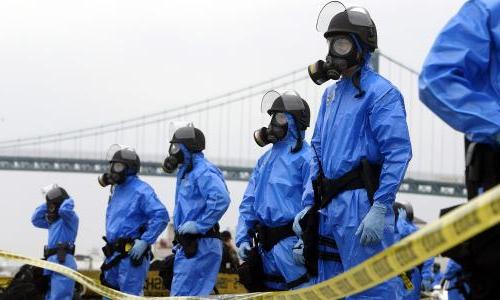 A line of people behind caution tape wearing nuclear contamination suits.